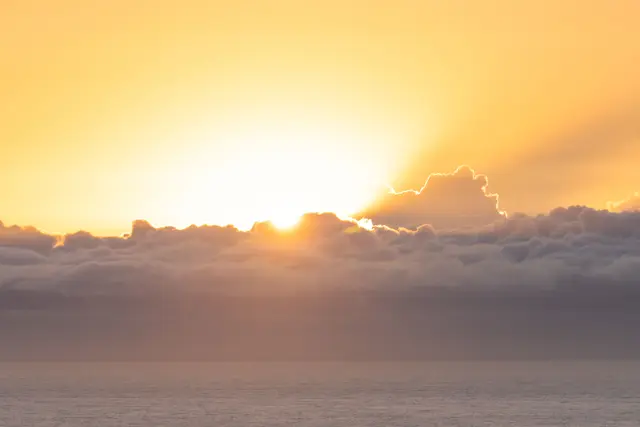 The sun breaking through a bank of dark clouds over the ocean at sunrise.