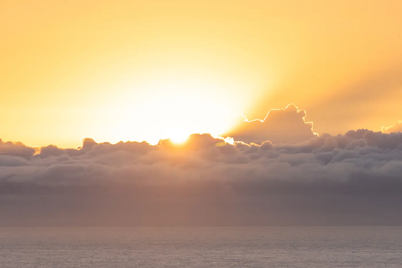 The sun breaking through a bank of dark clouds over the ocean at sunrise.