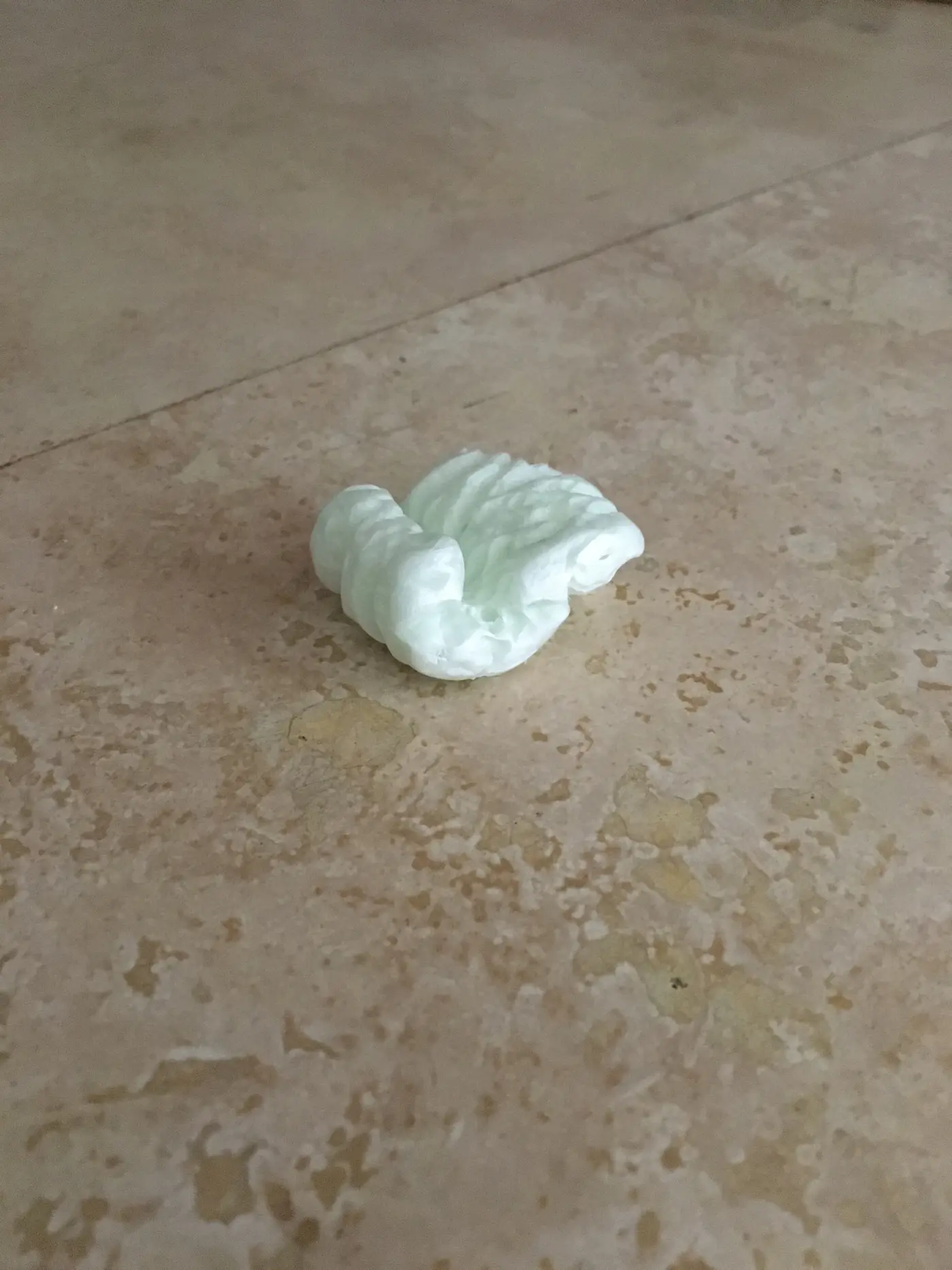 A small pale carved object resting alone on a tiled floor.