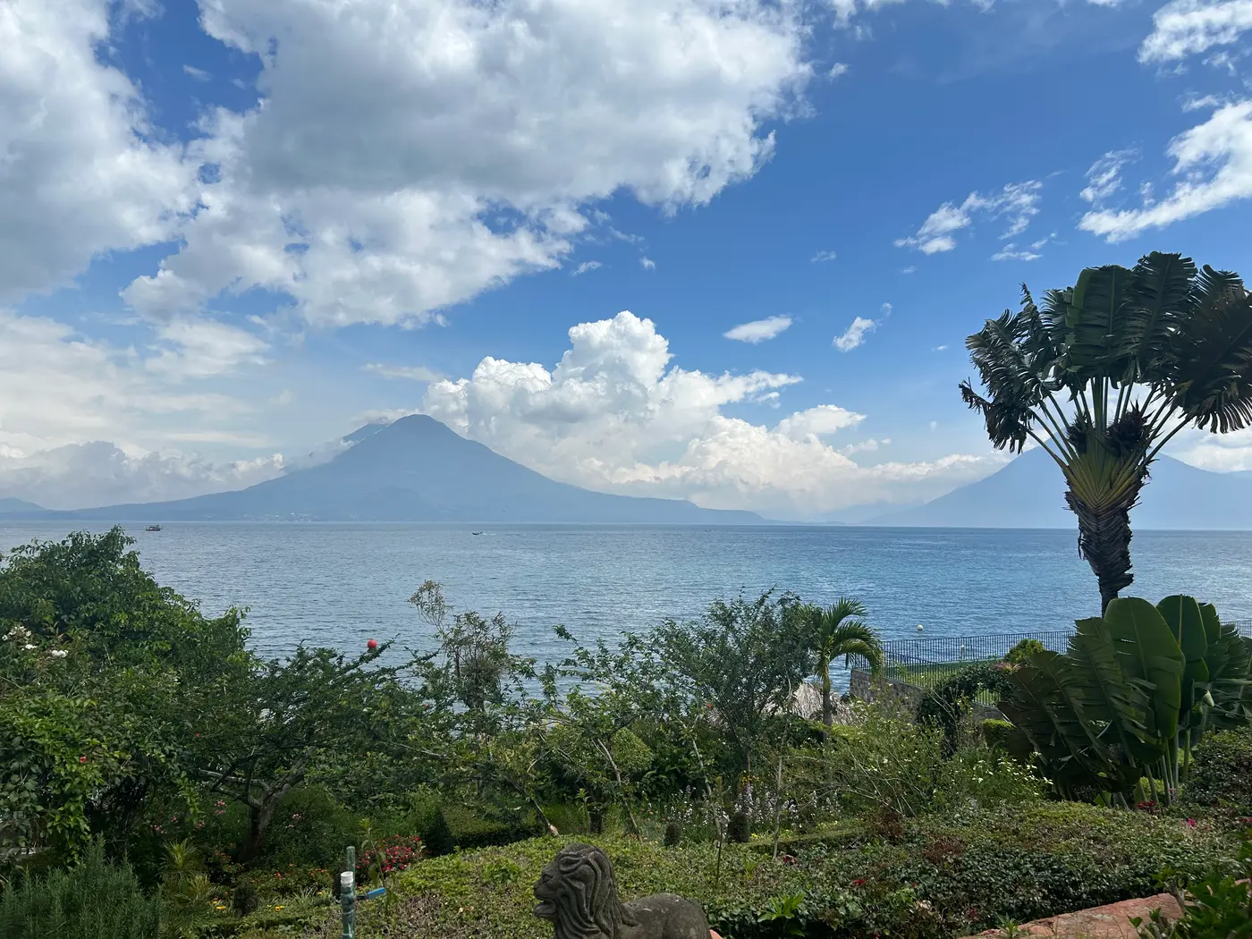 A garden overlooking Lake Atitlán in Guatemala, with a volcano rising above the water under a bright blue sky.