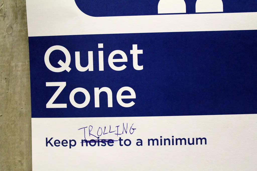A "Quiet Zone" sign where someone has crossed out "noise" and handwritten "TROLLING" above it.