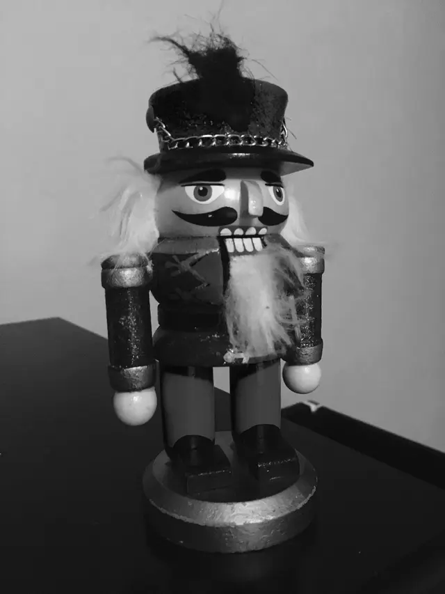 Black and white photo of a wooden nutcracker figure with a fur beard, standing on a table.