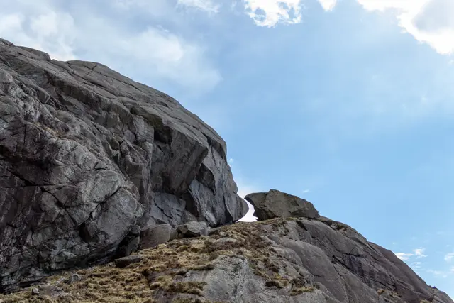 Massive weathered rock formation rising against a clear blue sky.